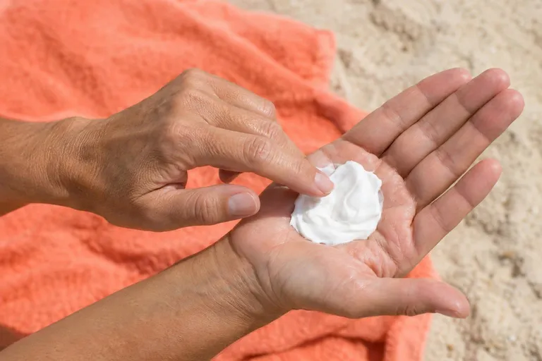 Twee handen op een koraalrode strandhanddoek, met een flinke klodder witte crème in de handpalm